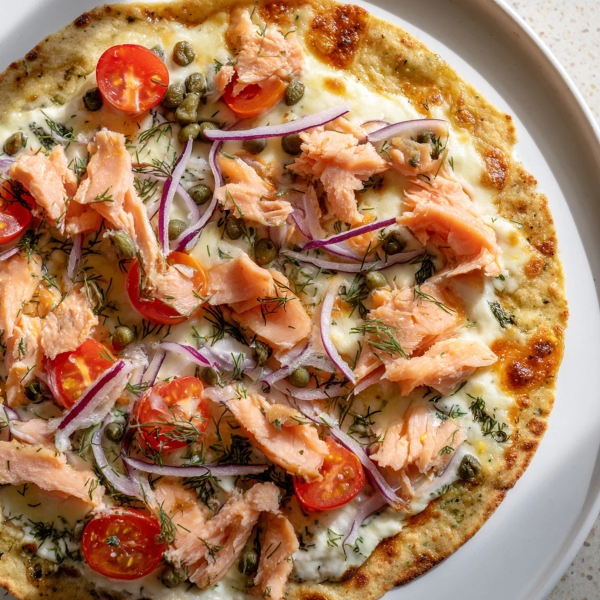 Golden baked salmon tortilla pizza topped with red onions, tomatoes, and bubbling cheese