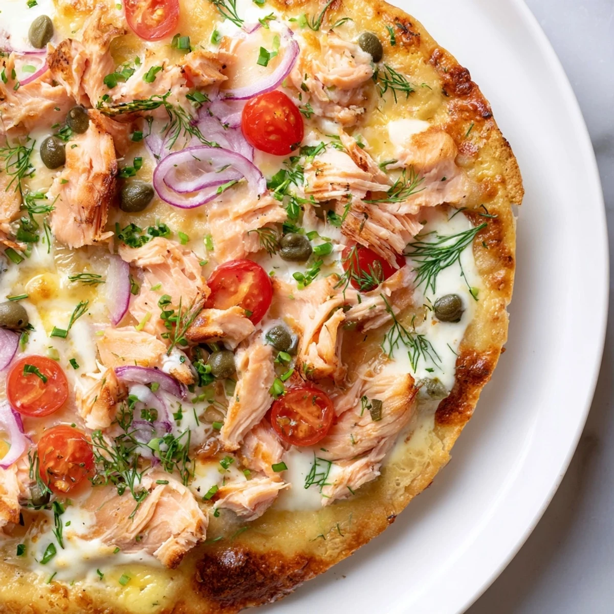 Creamy crème fraîche base on crispy leftover salmon tortilla pizza with capers and chives