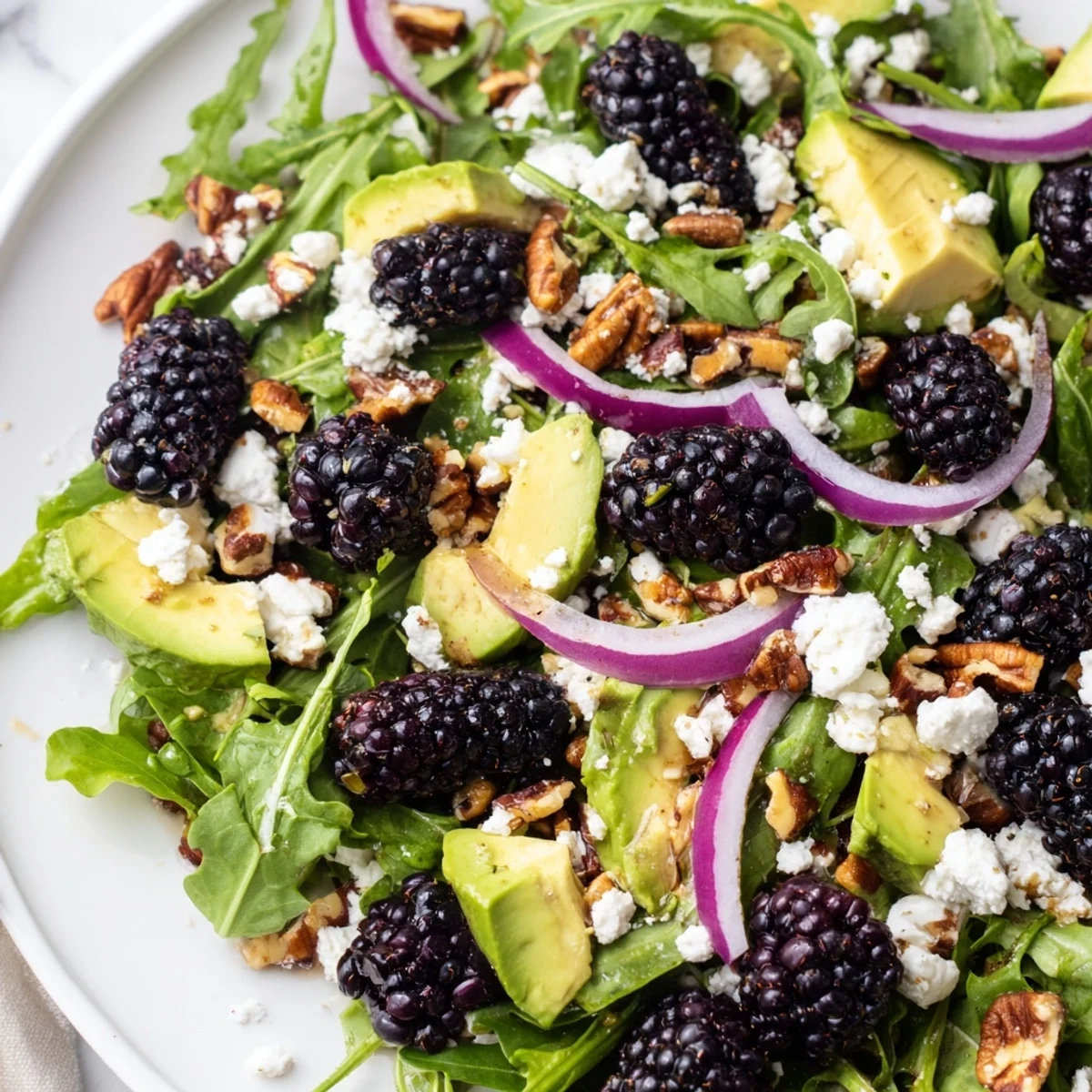 Colorful blackberry avocado salad topped with crunchy pecans and sliced red onion.