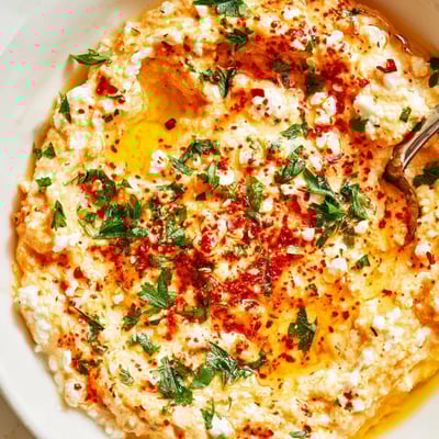 Spicy Greek Tyrokafteri feta dip garnished with parsley and drizzled olive oil on a white plate.