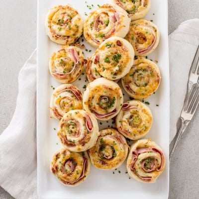 Freshly baked Ham and Cheese Pinwheels served warm, showcasing a crispy crust and savory ham filling perfect for parties.
