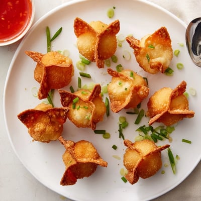 A close-up shows Crispy Crab Rangoon Bombs with Creamy Filling stacked beside a small bowl of sweet chili sauce.